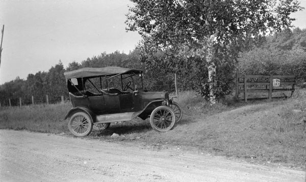 The photographer's automobile parked at the entrance to his cherry orchard. A sign on the gate offers a $25 reward for information on anyone stealing fruit.