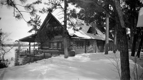 Winter view of the Hotz family cottage at Europe Lake, showing the massive chimney and rustic railing and lattice.