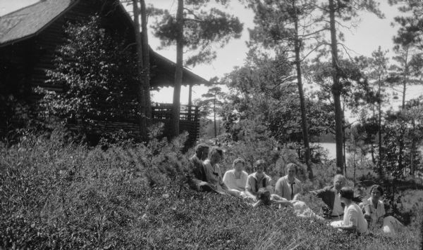 A group of men and women sit and recline on the hill beside the Hotz cottage.