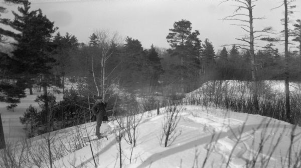 A man poses on snowshoes, using a long walking stick in a wooded, snow-covered landscape.