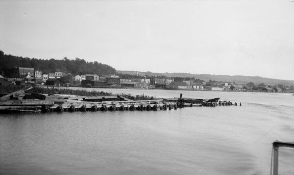 Elevated view over water of the harbor and buildings of Frankfort. There is a deteriorating pier in the foreground.