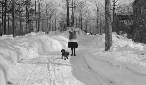 The photographer's daughter Margaret "Sissy" Hotz poses with a dachshund on the snowy driveway of the Hotz family home in Glencoe, Illinois.  There are other children in the background.