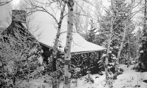 One of the Hotz Fish Creek cottage stands covered with snow among birch and evergreen trees.
