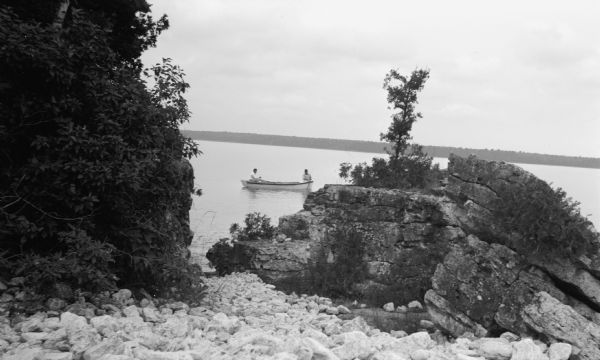 View from rocky shoreline of two men fishing from a small boat near Toft Point.