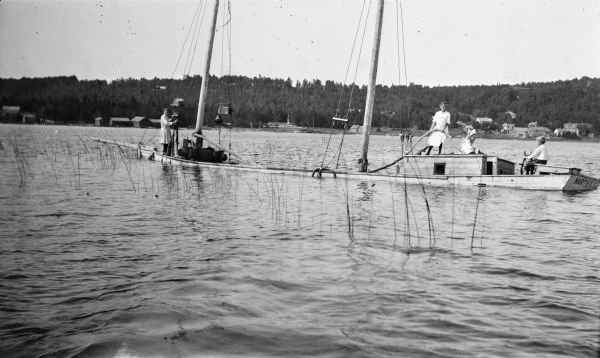 The photographer's daughters, from left, Helen, Alice, Margaret and son Ferdinand Leonard at the wheel, pose on a two-masted boat, the <i>Martha G.</i>, which has run aground in shallow water near Fish Creek. There are houses and other buildings on the far shoreline.