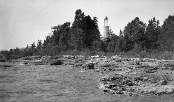 The Baileys Harbor Light as seen from the water. The lighthouse, with a tapered cylindrical stone base, birdcage lantern, and copper dome, was deactivated in 1869. It was replaced by the Baileys Harbor range lights and the Cana Island lighthouse.