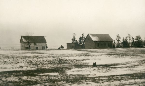 View across snowy field of a shingled house, barn and other outbuildings standing empty near the shore of Lake Michigan at Newport Village.