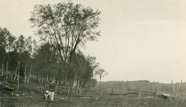 A woman and girl pose near a wooden fence that separates a field from a stand of birch trees.