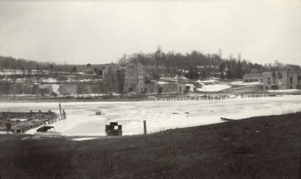 View of the large abandoned furnace complex, left, company store, far right, and blacksmith shop behind the company store, on the site of the Jackson Iron Company, which closed in 1891. A boat is moored along the shore in the foreground.