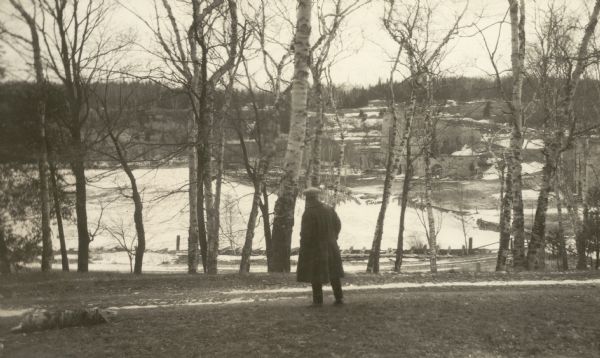 An unidentified man looks across Snail Shell Harbor at the remains of the Jackson Iron Company works. The large furnace complex is visible through the trees.
