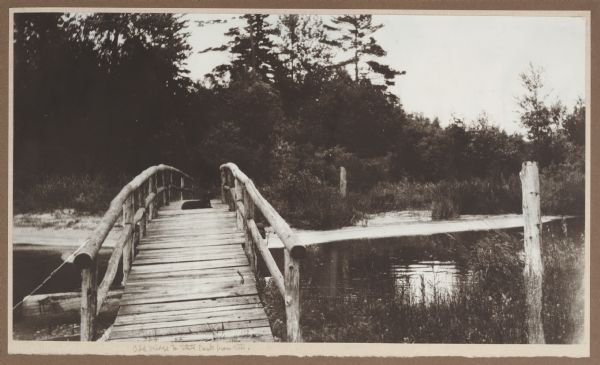 View from the Vits property, looking east, across a rustic foot bridge over Fish Creek leading to Peninsula State Park. A dachshund rests in the middle of the bridge.