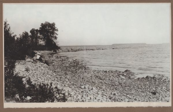 An unidentified child sits on the rocky shore at Weborg Point. Big Strawberry Island is seen center right, with Chambers Island on the horizon to the left.