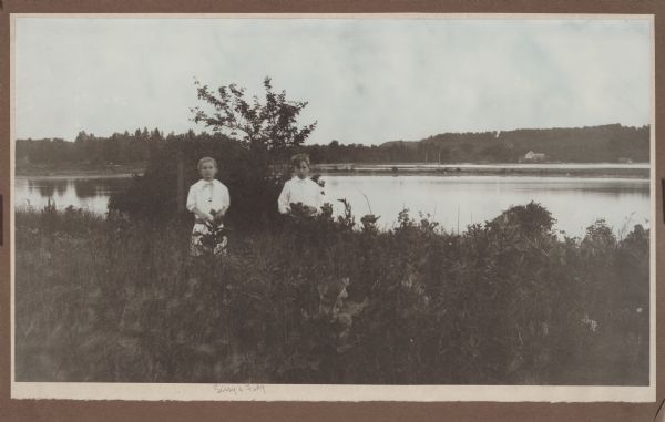 Two of the photographer's children, Margaret (Sissy), left, and Ferdinand Leonard (Fedy), right, on Weborg Point. Fish Creek Harbor is in the background; the Hotz boathouse, with white door, and bathhouse are seen at extreme right.