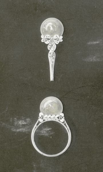 A drawing on grey cardboard of a design for a ring featuring a large pearl. The mounting, of white gold or platinum, features smaller stones and a bowknot design.