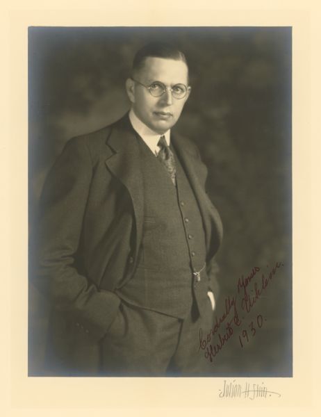 A signed and dated three-quarter length standing studio portrait of Milwaukee businessman Herbert E. Uihlein (1890-1947), son of Alfred Uihlein, president of the Joseph Schlitz Brewing Company. He is wearing a three-piece suit with watch chain and fob.