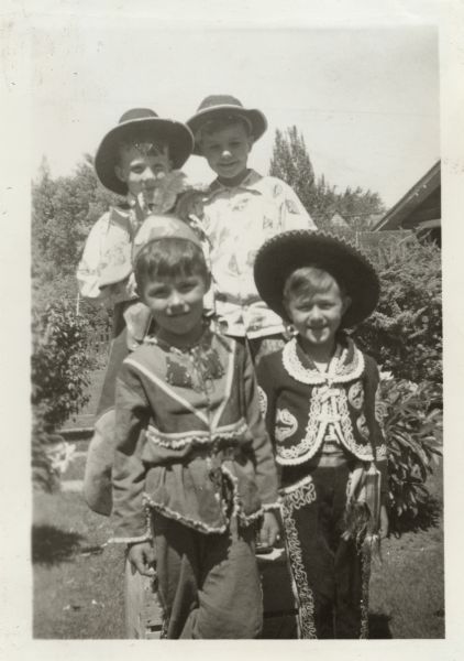 Four boys posing in Robert E. Faber's (b. 1933) backyard in the 2500 block of Van Hise Avenue, Madison, Wisconsin.  They are, clockwise from bottom left, Bill Marshall in an Indian costume, Jim Marshall (Bill's brother) in a cowboy costume, John Scherrer in a cowboy costume, and Robert E. Faber in a Mexican cowboy costume.