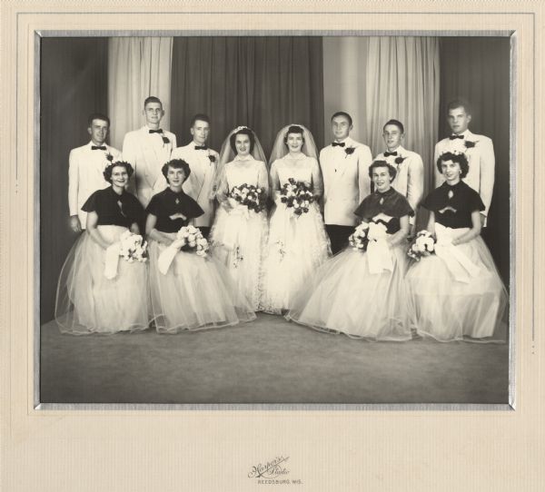 A studio portrait of a double wedding. The wedding was held September 19, 1953 in Reedsburg, Wisconsin.

On the right is the wedding party of Norbert Meyer (b. 1929) and Lorraine Krueger (1932-2007). The bridesmaid seated second from the right is Elderene Halvensleben (1932-2011), who married Vernon Hasz (1927-1988) the following year.
