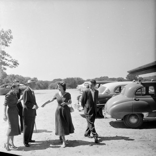 Frank Lloyd Wright and Olgivanna Lloyd Wright arriving at the First Unitarian Society Meeting House where he was to deliver a speech. The speech was to be broadcast as part of the Omnibus television program. However, the speech was not aired as part of Wright's live television interview. The other people in the photograph have not been identified.