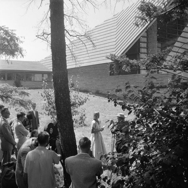 Frank Lloyd Wright on the grounds of the First Unitarian Society meeting house.  Wright was being filmed for the Omnibus television program. The woman with Wright is apprentice Frances Nemtin. The other people in the photograph have not been identified.