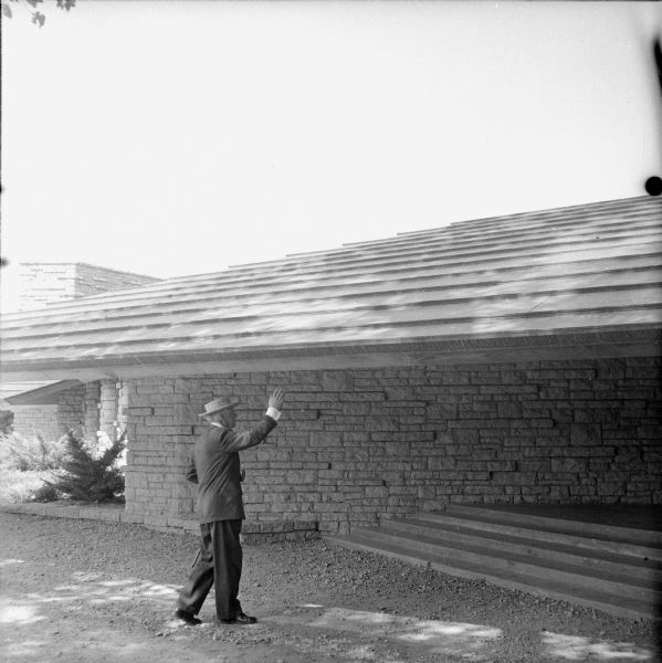 Frank Lloyd Wright at the entrance to the First Unitarian Society Meeting House, apparently pointing out the low overhang of the roof. Tradition says the overhang was originally even lower, but the entrance was regraded after Wes Peters, Wright's tall chief apprentice, hit his head.