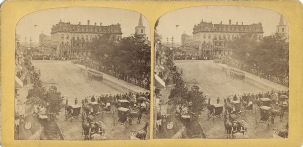 Stereograph of view of procession, military company and citizens at Great Centennial Day at the Capitol Square. Scene at Main and Carroll Streets showing the Park Hotel and the spire of the Baptist Church in the background. Elevated view taken from Vilas House towards Park Hotel.