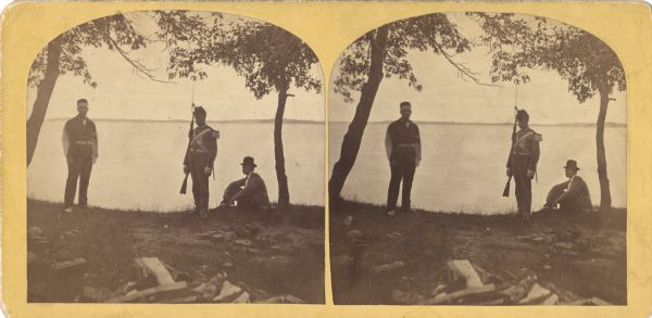 Three men on shoreline of Lake Mendota, one wearing a military uniform like those worn during the 1876 Centennial Celebrations in Madison. The location appears to be near Tenney Park, Maple Bluff. At the right, the State Asylum for the Insane is on the far shoreline.