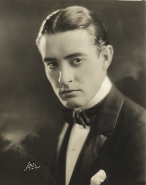 Quarter-length studio portrait in front of a painted backdrop of actor John Gilbert wearing a tuxedo.