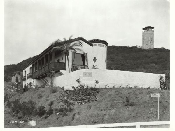 Exterior view of actor John Gilbert's Spanish-style house at 1400 Tower Grove Road. There is a tower on the hill in the background.