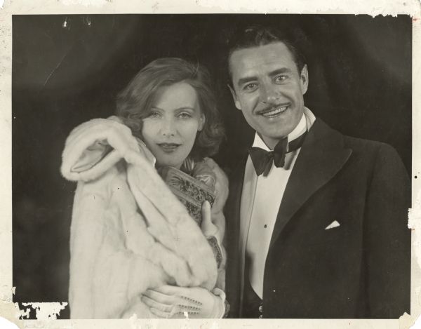 John Gilbert and Greta Garbo pose for photograph at the premiere of their film "The Flesh and the Devil." She is wearing a fur coat, white gloves and is holding a purse; he's in a tuxedo and overcoat.