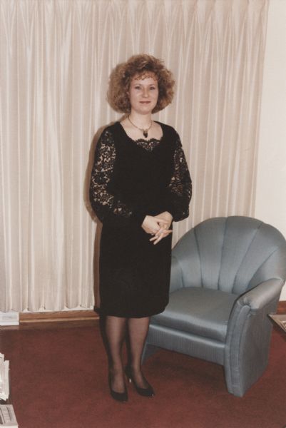 Jill Bremigan in a black velvet and lace cocktail dress that she made from Butterick pattern 6402 (1992). She wore it to a Christmas party held in Madison, Wisconsin, by the company her husband, Cary Bremigan, worked for at the time. Jill's hands are clasped in front.