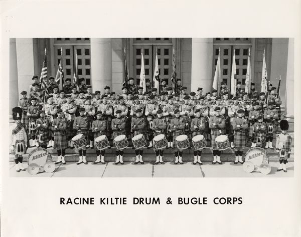 A group portrait of the Racine Kiltie Drum & Bugle Corps. They are all posed with their instruments and wearing their uniforms. The uniforms have a Scottish theme with kilts. For names of the band members, see the Public Note.