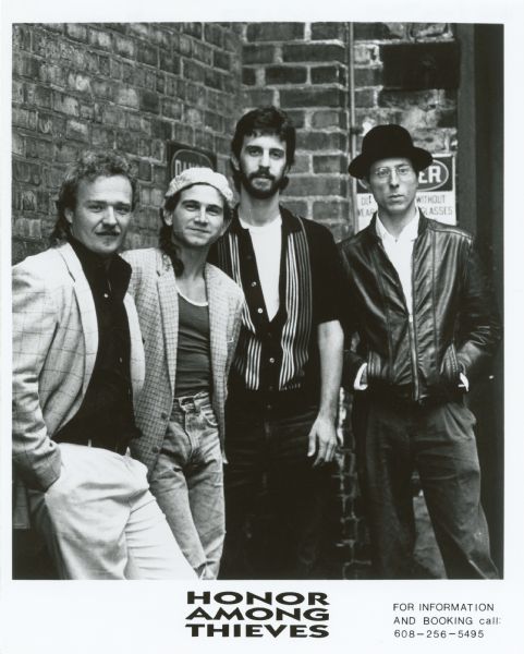 Publicity photograph of the four band members from Honor Among Thieves, a Madison, Wisconsin rock band. From right to left are Pat Dieter, Doug DeRosa, Joe Parisi, and Andy Ewen. The band is standing in front of a brick wall.