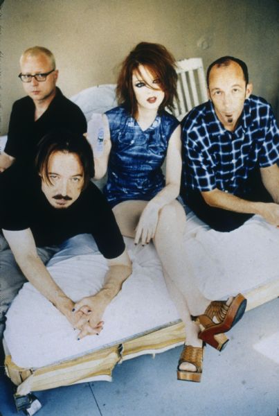 Color publicity photograph of the band members from Garbage, a Madison, Wisconsin rock band. From left to right are: Butch Vig, Steve Marker, Shirley Manson, and Duke Erikson. They are sitting or leaning on a bed with white linens.<p>Almo Sounds is mentioned on the slide.