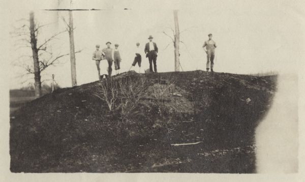 Three men and four children standing on top of a mound near Round Lake.