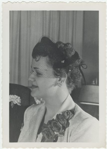 Quarter-length portrait of a bride showing the brilliant studded veil of her black shell hat and her earrings. Her corsage was of red roses.