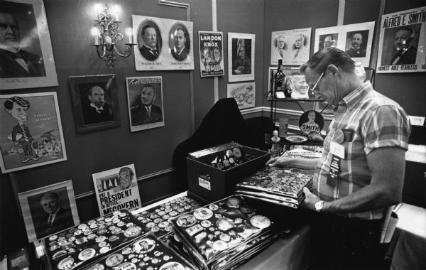 Don Starky, of Napoleon, Ohio, looks over some of the buttons on display at the American Political Items Collectors Association Convention. Political posters are hanging on the wall, and other items can be seen on a shelf.