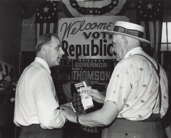 A straw hatted fairgoer from Oshkosh clutched Republican leaflets as he tried to straighten out State Senator Gaylord Nelson on world affairs. Nelson, Democratic candidate for governor, had wandered from the Democratic booth at the state fair and stopped to shake hands at the Republican booth in the same building.
