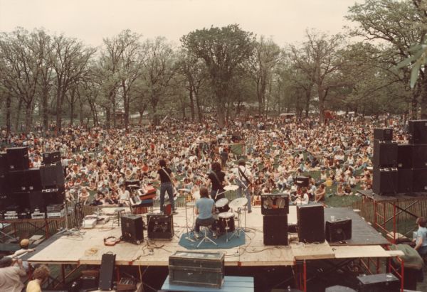 View from above and behind the stage as the band, Spooner, performs at the MadCity Music Festival held at Olin Park, Madison, Wisconsin. Band members included Butch Vig (drums), Duke Erikson (keyboard), Dave Benton (bass), and Bob Olsen (guitar).