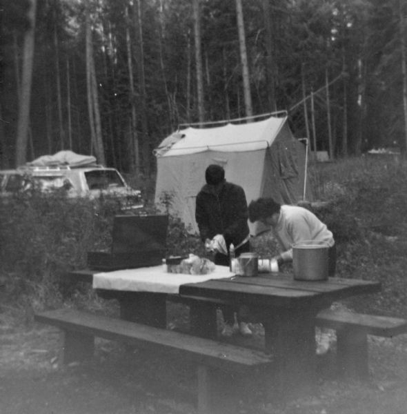 Donald Soehnlein took this photograph while on vacation in the Bitterroot Mountains, near Lola, Montana. It depicts his wife Nina and son James cleaning up the breakfast dishes on a picnic table in front of the family tent and car, a 1966 Plymouth Belvedere II. The camping cook set depicted was made by the Mirro Aluminum Company and is in the Wisconsin Historical Society Museum collection. The Soehnleins took family camping vacations out West as well as around Wisconsin.
