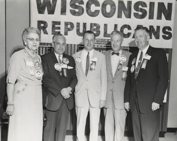 Wisconsin Republicans stand for their portrait at a reception while attending the Republican National Convention. They are wearing buttons for "Byrnes for Veep" and "Kuehn," and also their convention badges with ribbons. Names, left to right: Mrs. Glenn Wise (Wisconsin's first woman Secretary of State), unknown man, Philip G. Kuehn (running for Governor of Wisconsin), Warren P. Knowles (future Governor of Wisconsin), and Leo Rothe.