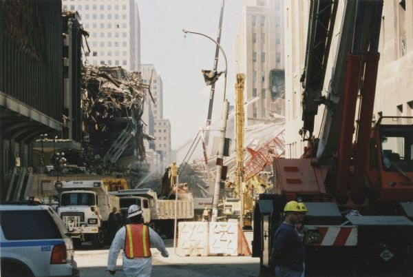 World Trade Center debris piles on Vesey Street, looking west. On the left are World Trade Center buildings 5 and 6 which were heavily damaged by the collapse of North Tower, and on the right the debris pile of World Trade Center building 7 which collapsed late in the afternoon of September 11.