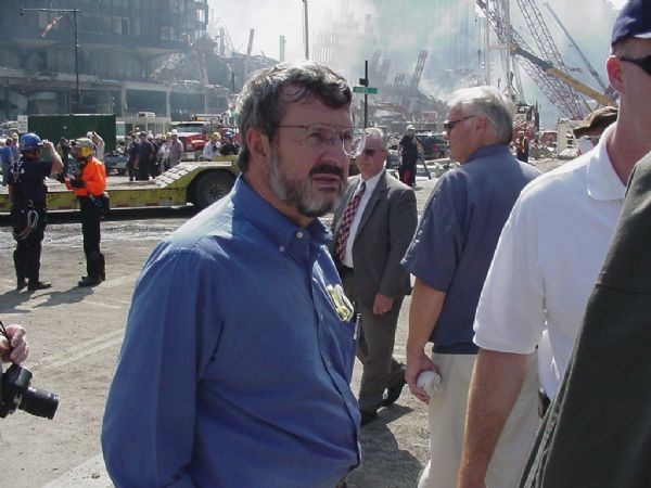 Wisconsin Congressman David R. Obey, wearing a blue shirt, is standing in the foreground. Behind him, also in a blue shirt, is Florida Congressman Bill Young. They are, respectively, the ranking Democrat and Republican chair of the House Appropriations Committee. Obey and Young were there to see the site at the World Trade Center shortly after the 9/11 attack first-hand. Obey and Young are standing at the intersection of Vesey Street and the West Side Highway. Behind them are the ruins of World Trade Center Building 6 (6 WTC)and the debris pile of the North Tower.