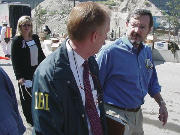 Wisconsin Congressman David R. Obey (right) touring the World Trade Center Ground Zero site a few days after the 9/11 attack. Obey was there as the senior Democrat on the House Appropriations Committee.  With Obey is an unidentified FBI officer. The woman in the background is also unidentified. She is wearing a 9/11 "never forget" ribbon.  Further in the background, on what is thought to be the West Side Highway, is a large dust pile.