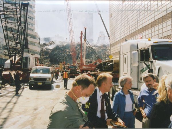 Wisconsin Congressman David R. Obey (right, in the blue shirt) touring the 9/11 Ground Zero site with an unidentified FBI official, Joan Obey, and an unidentified individual in a dust mask. As the leading Democrat on the House Appropriations Committee, Obey was in New York City only a few days after 9/11 to review plans for the cleanup. In the background is the debris pile of the World Trade Center, which collapsed during the afternoon of 9/11, and the damaged facade of the building of 30 West Broadway.