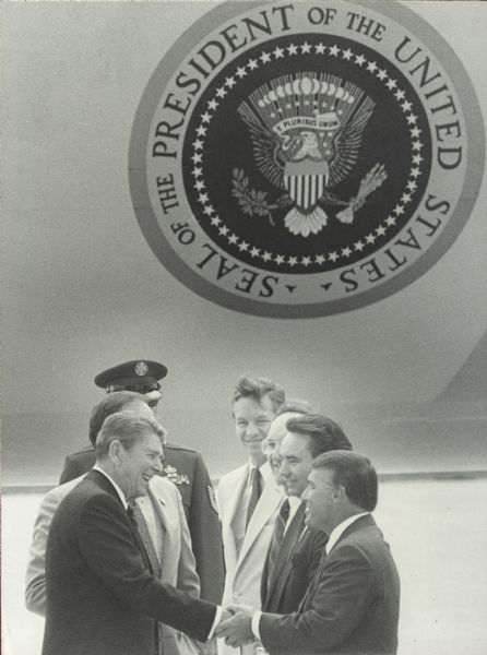 State Senator Michael Ellis shakes hands with President Ronald Reagan. Governor Tommy Thompson is standing next to Ellis. Air Force One with the seal of the President appears in the background.