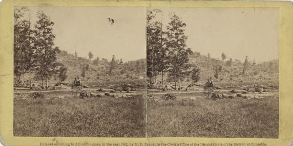 Stereograph of a scene near the site of the Gettysburg battlefield. Two men sit in a wagon in the center of the image.