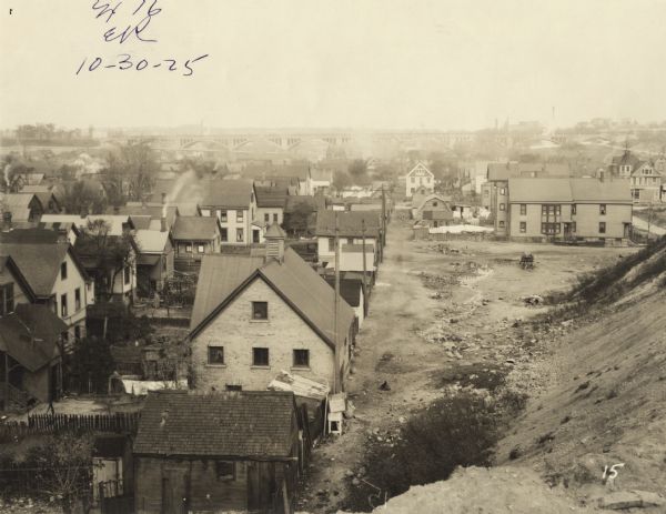 Elevated view of alley between houses in a neighborhood from railroad embankment. An elevated bridge is just visible in the far background. Text at foot of photograph reads, "Alley Between 39th & 40th. 19+70 Looking North from Line." Handwritten in ink at top, "Ex. 16, ER, 10-30-25."