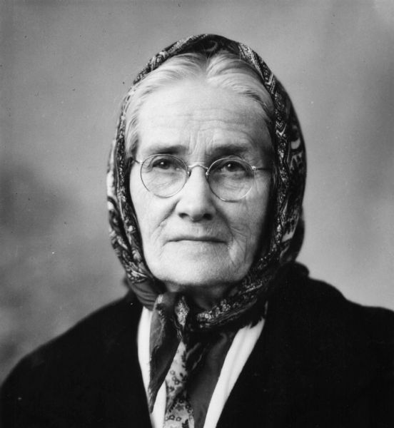 Quarter-length portrait of Ingeborg Sidwell wearing a patterned scarf, tied under her chin, a dark coat and eyeglasses. In 1943, she was working at the Wisconsin State Capitol as a scrubwoman. She was 79 years old and wanted to retire, but knew it would be difficult. She lost all of her money when the banks failed in the 1930s. When Governor Goodland vetoed the state employee's pension bill, she worried about what would happen, not only to herself but her coworkers. They were all elderly and most had medical issues. So, she sought out the governor and told him of the small salary she made, her many expenses and her small savings. She asked him to reconsider. Whether her chat with the governor made the difference is unknown. However, not long after their meeting, the governor sent a message to the Legislature asking that they override his veto, which they did. Ingeborg received a monthly pension of $14.70. She died in 1947 at the age of 84.