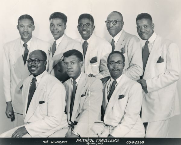 Group portrait of the Faithful Travelers. Eight African American men, three in front, five in back, pose wearing light suits, dark neckties and pocket kerchiefs. Several men wear eyeglasses. Text appears in a dark bar across the bottom that reads: "Faithful Travelers, 915 W. Walnut, Milw., Wis., C040269."