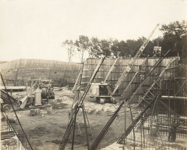 Elevated view of a building site with "O'Dea and Shafer, Engineers and Contractors" construction crew, crane and other equipment. On the photograph album binding on the left side of the photograph is written "Reservoir at Madison."